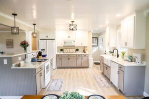 Une cuisine moderne avec des meubles blancs, un îlot central, des luminaires suspendus et un panneau « Détendez-vous » accroché au mur.