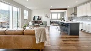 A spacious living room with a large sofa, a television, and a dining area with chairs and a kitchen with white cabinets and a bar. - Sedona Sky View (Sedona)