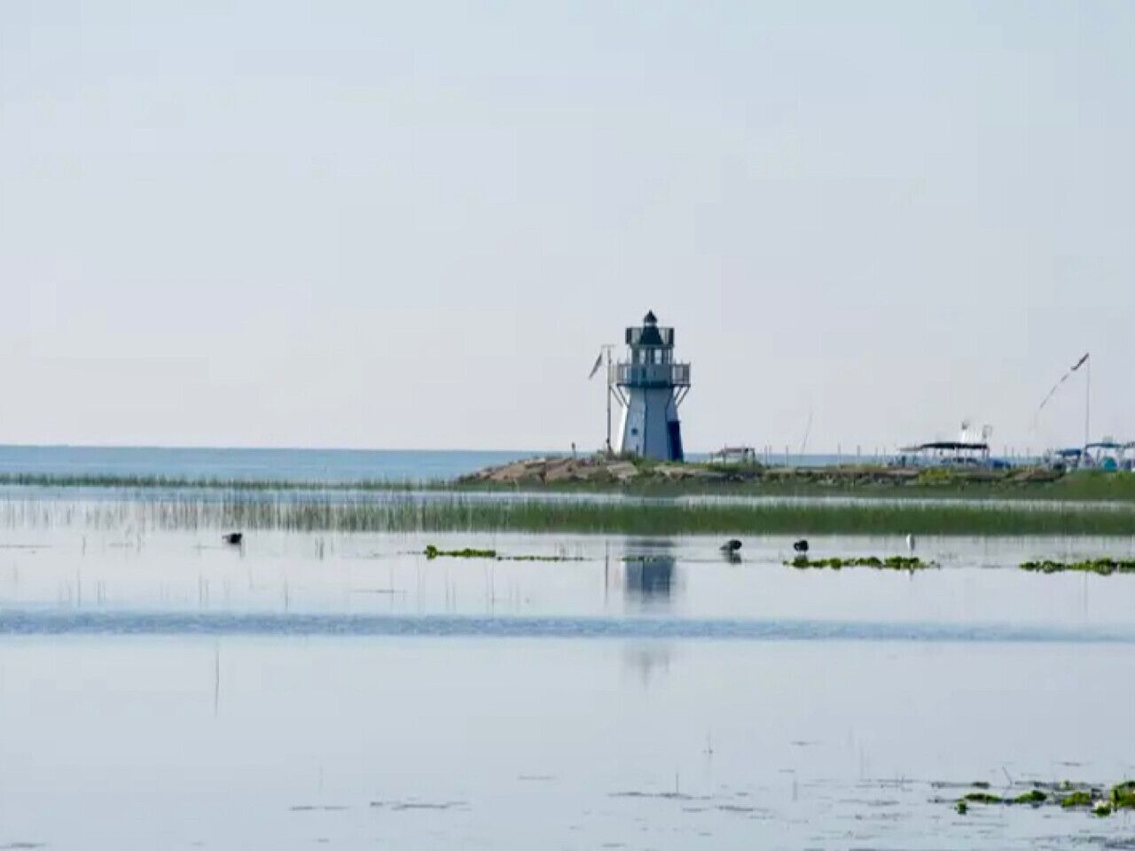 A lighthouse on a small island with calm water and sparse vegetation.