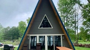 Eine dreieckige A-Form-Hütte mit einer Terrasse, Sitzgelegenheiten im Freien und einem Grill.
