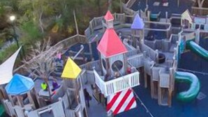 Um parquinho com diversas estruturas de lazer, incluindo escorregadores, áreas de escalada e uma pequena torre.