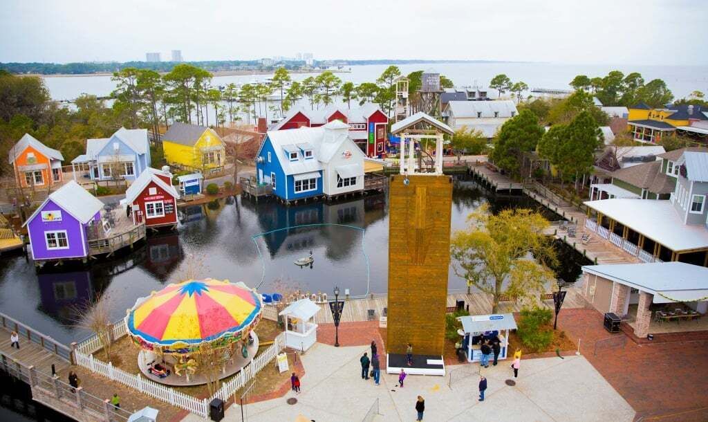 A waterfront area with colorful buildings, a central wooden structure, and a carousel.
