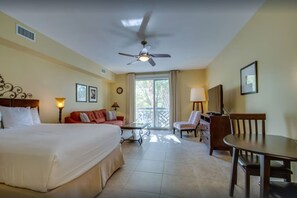 Una habitación de hotel con cama, sofá, televisor, mesa de comedor y ventilador de techo.