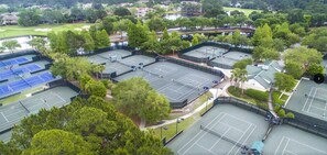 Vista aérea de un complejo de tenis con varias canchas rodeadas de árboles y un lago.