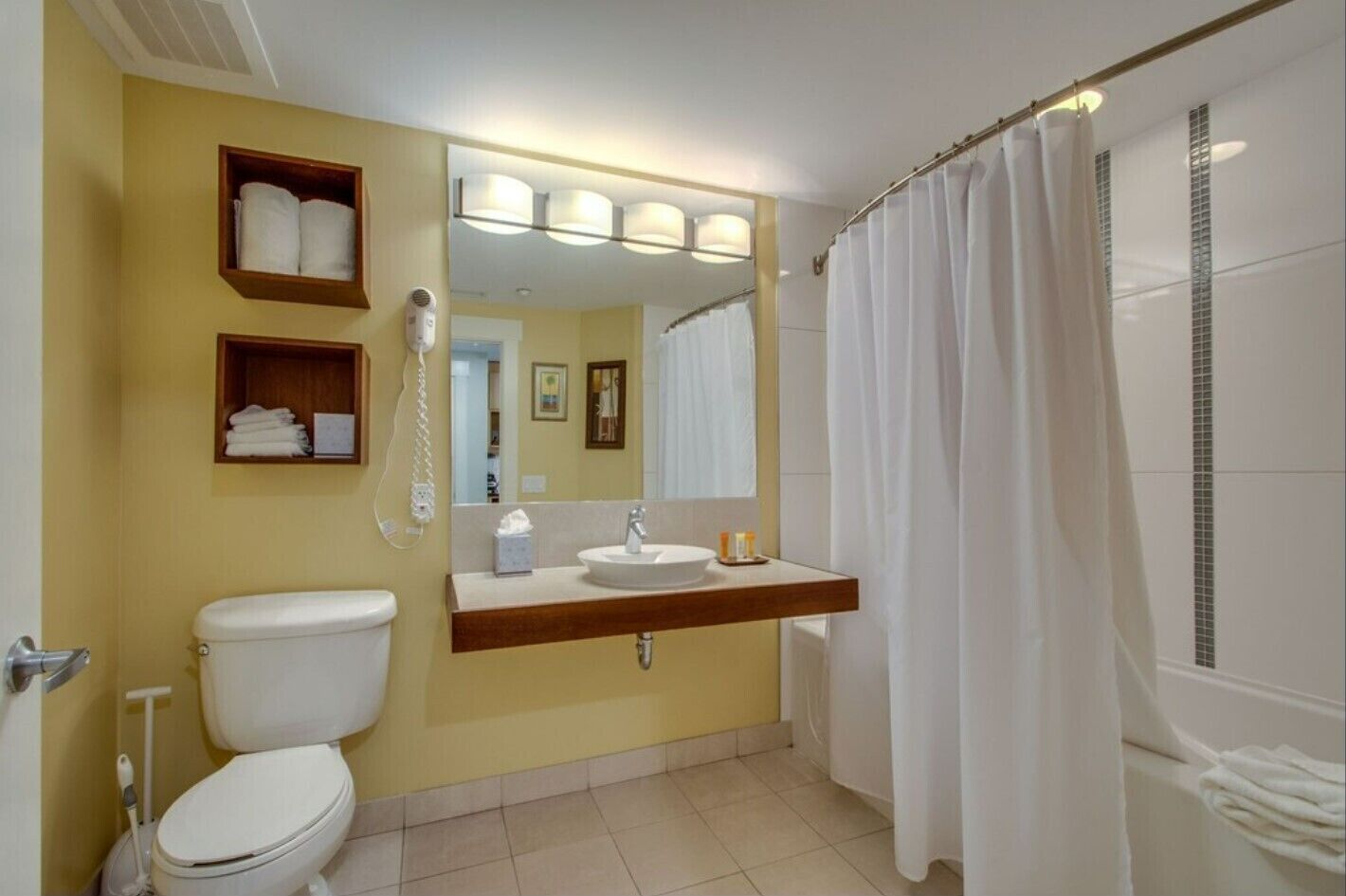 A bathroom with a toilet, sink, and shower. There are towels on a shelf and a phone on the wall.