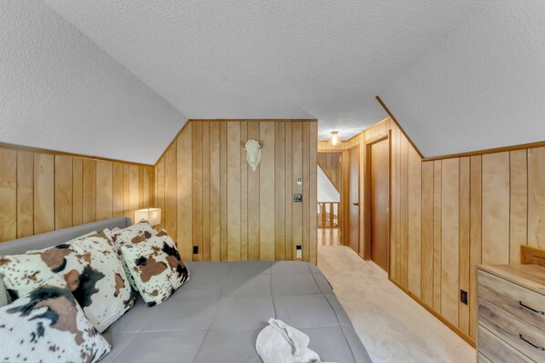 Un dormitorio con techo de madera, una cama con almohadas estampadas, una toalla blanca y un aparador de madera.