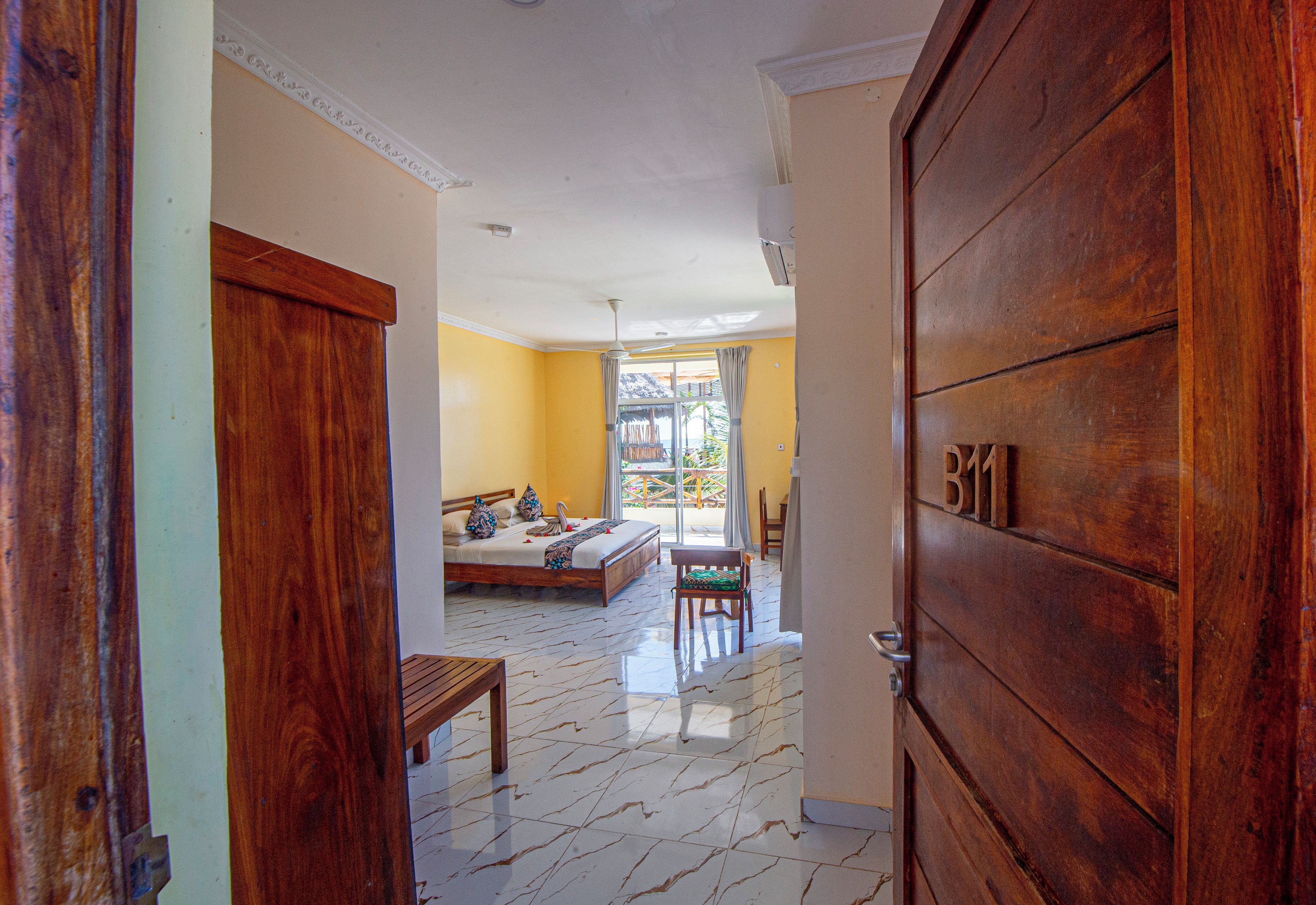 A hotel room with a bed, a wooden bench, a dining table, and a view of the outdoors.