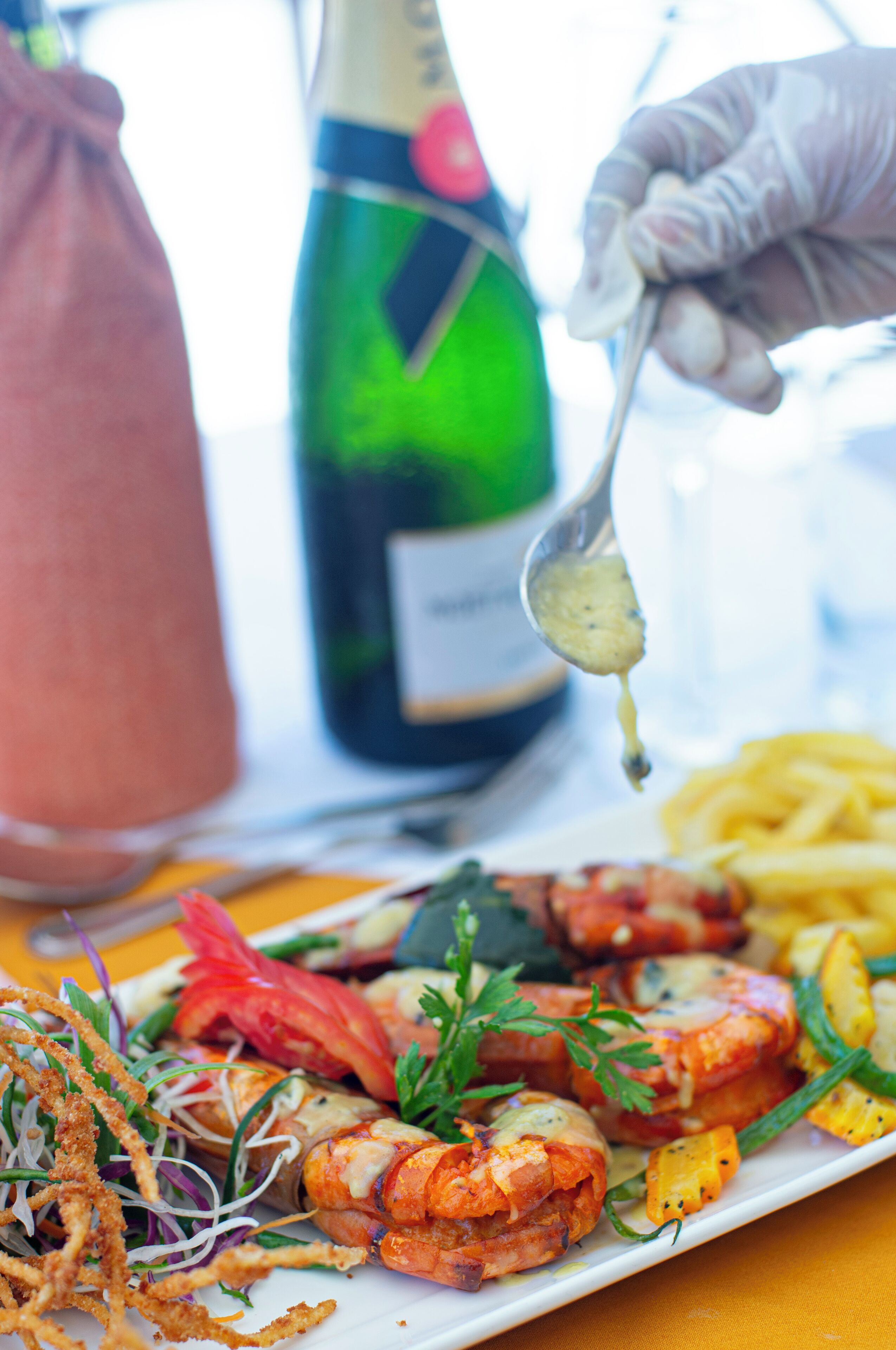 A plate of food with shrimp, vegetables, and fries, and a bottle of champagne in the background.