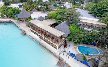 A resort with a pool, thatched-roof buildings, and a beachfront view.