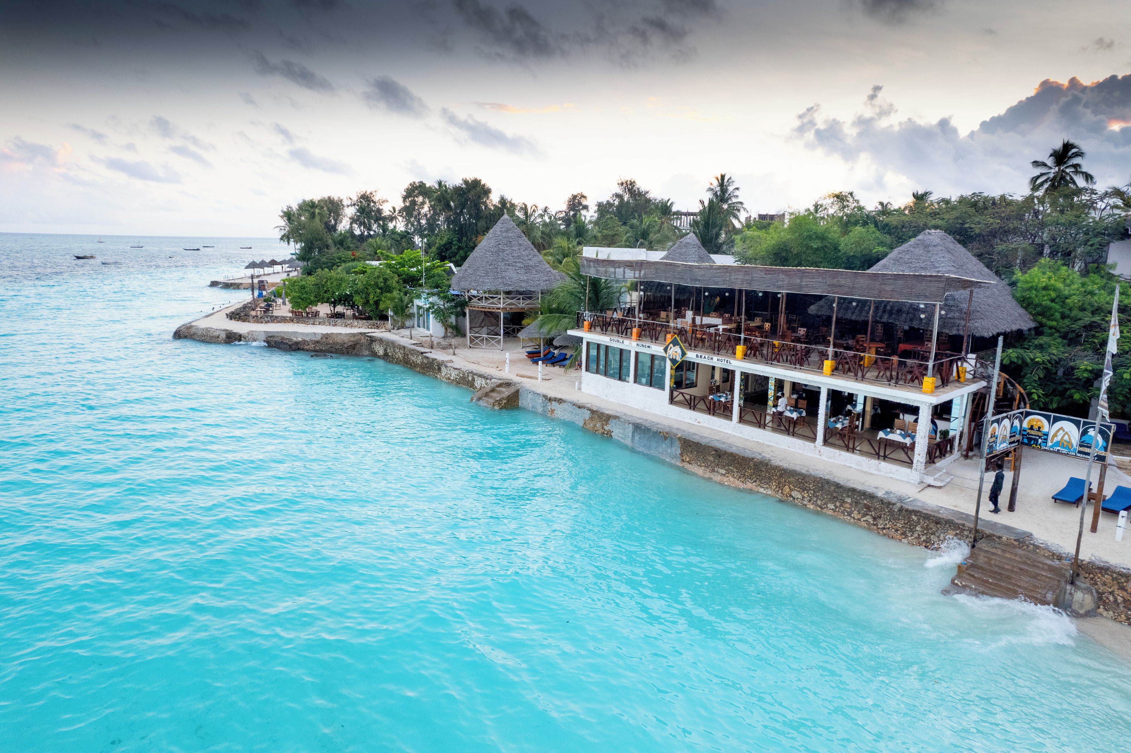 Un hotel frente al mar con bungalós sobre el agua, una piscina y un bar en la playa.
