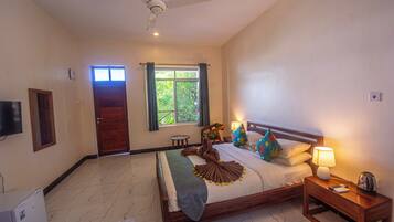 A hotel room with a bed, a nightstand, a ceiling fan, a window with curtains, and a door.