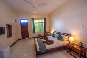 A hotel room with a bed, a nightstand, a ceiling fan, a window with curtains, and a door.