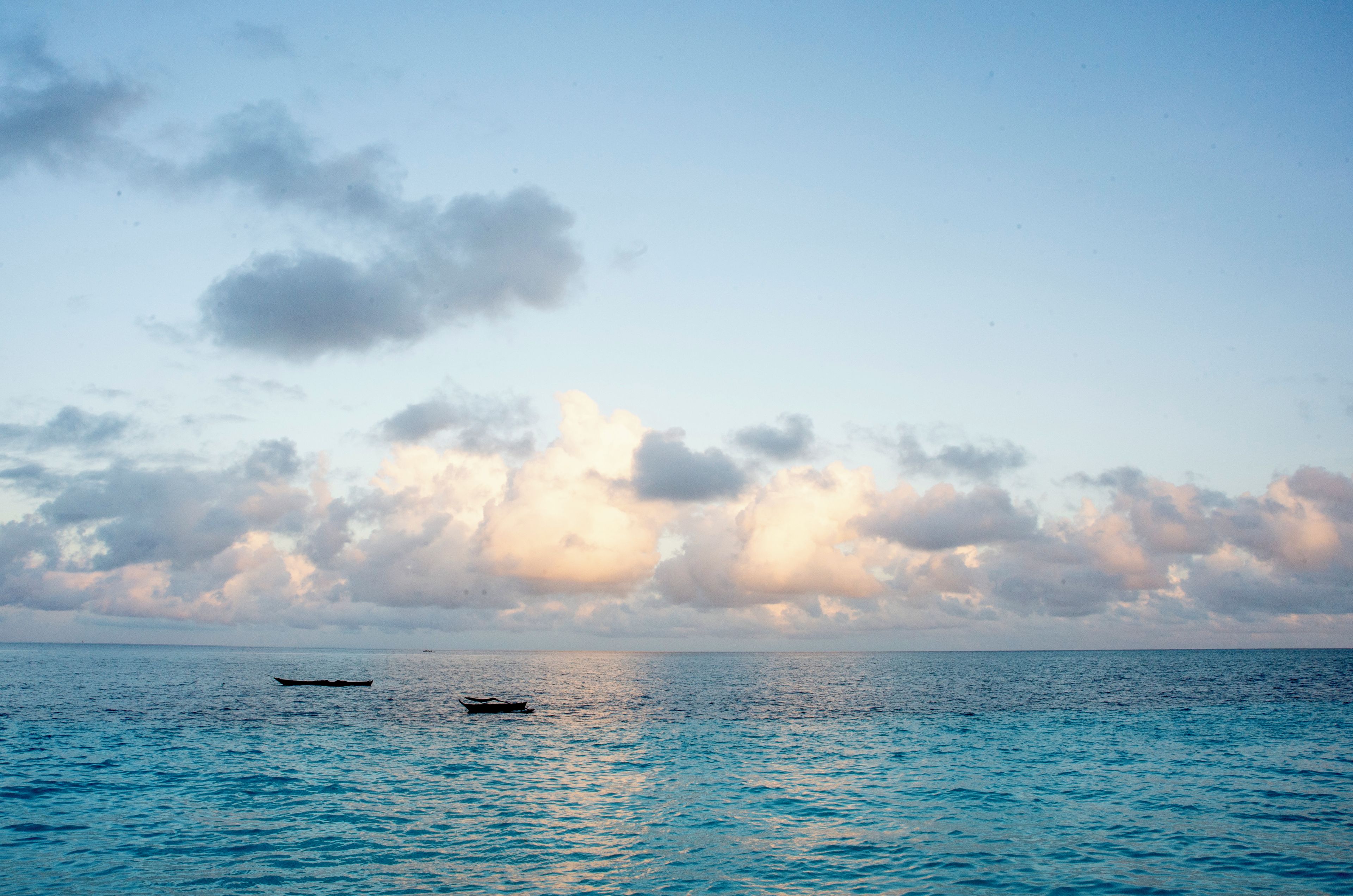 A calm sea with two boats and a partly cloudy sky.