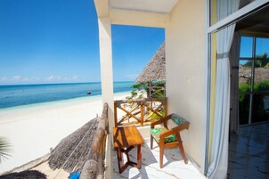 A beach view from a room with a wooden bench and a thatched roof structure.