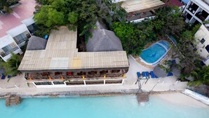 Eine Luftaufnahme eines Resorts mit Pool, Strand und mehreren Gebäuden mit Strohdächern.