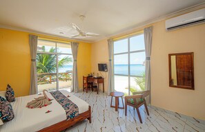 A hotel room with a bed, a desk, a chair, and large windows overlooking the sea. - Double A Nungwi Beach Hotel – Beach Front (Nungwi)