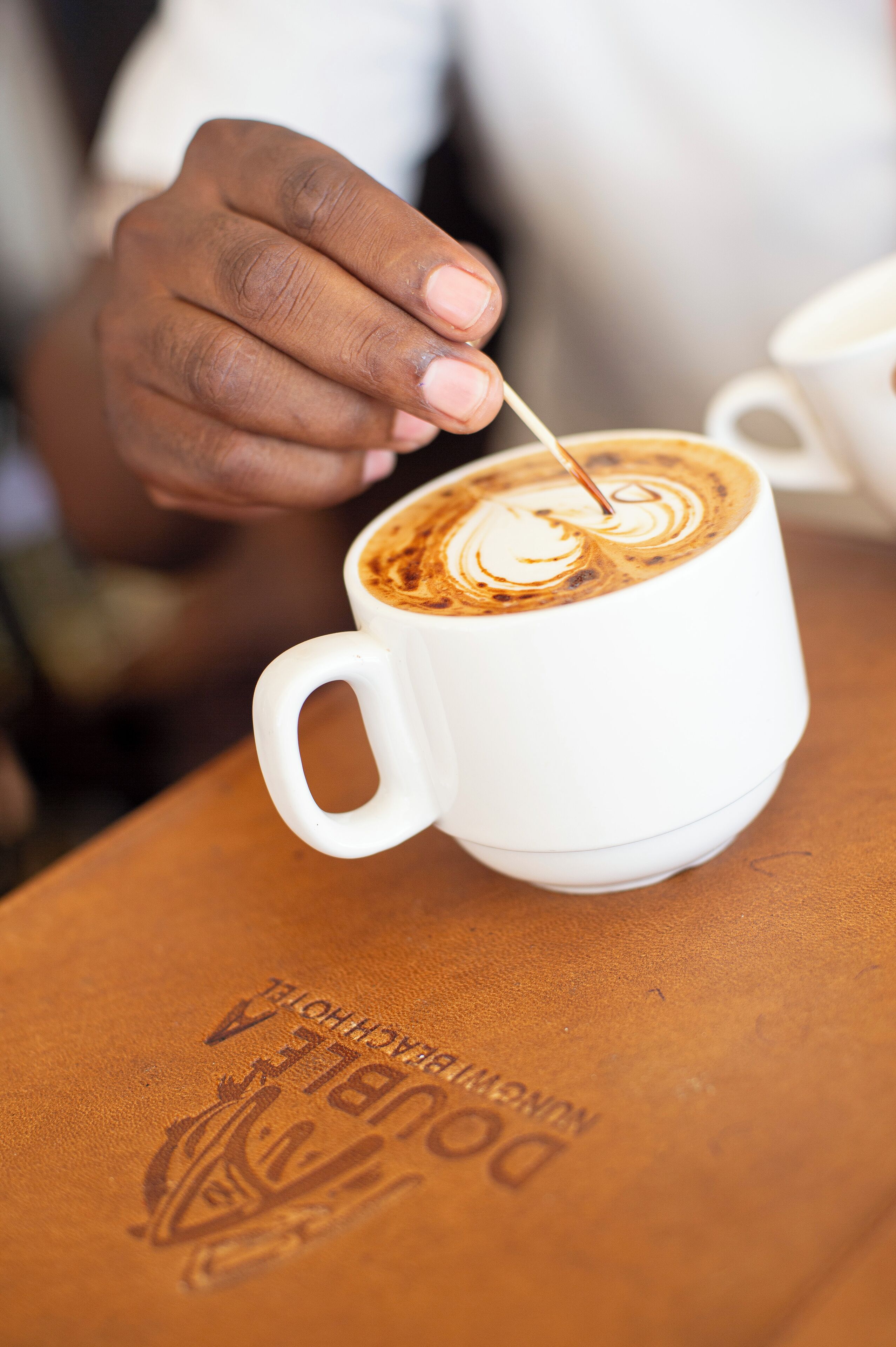 Een detailfoto van een hand die een kop koffie met latte-art roert.