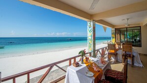 Ein Restaurant direkt am Strand mit Blick auf das Meer, ausgestattet mit einem Essbereich, Tischen, Stühlen, einem Mülleimer und einem Deckenventilator.