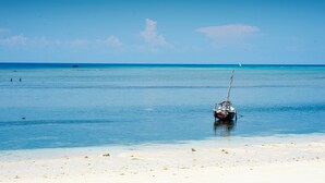 Ein Boot ankert in einem klaren, blauen Meer, im Vordergrund ein Sandstrand.