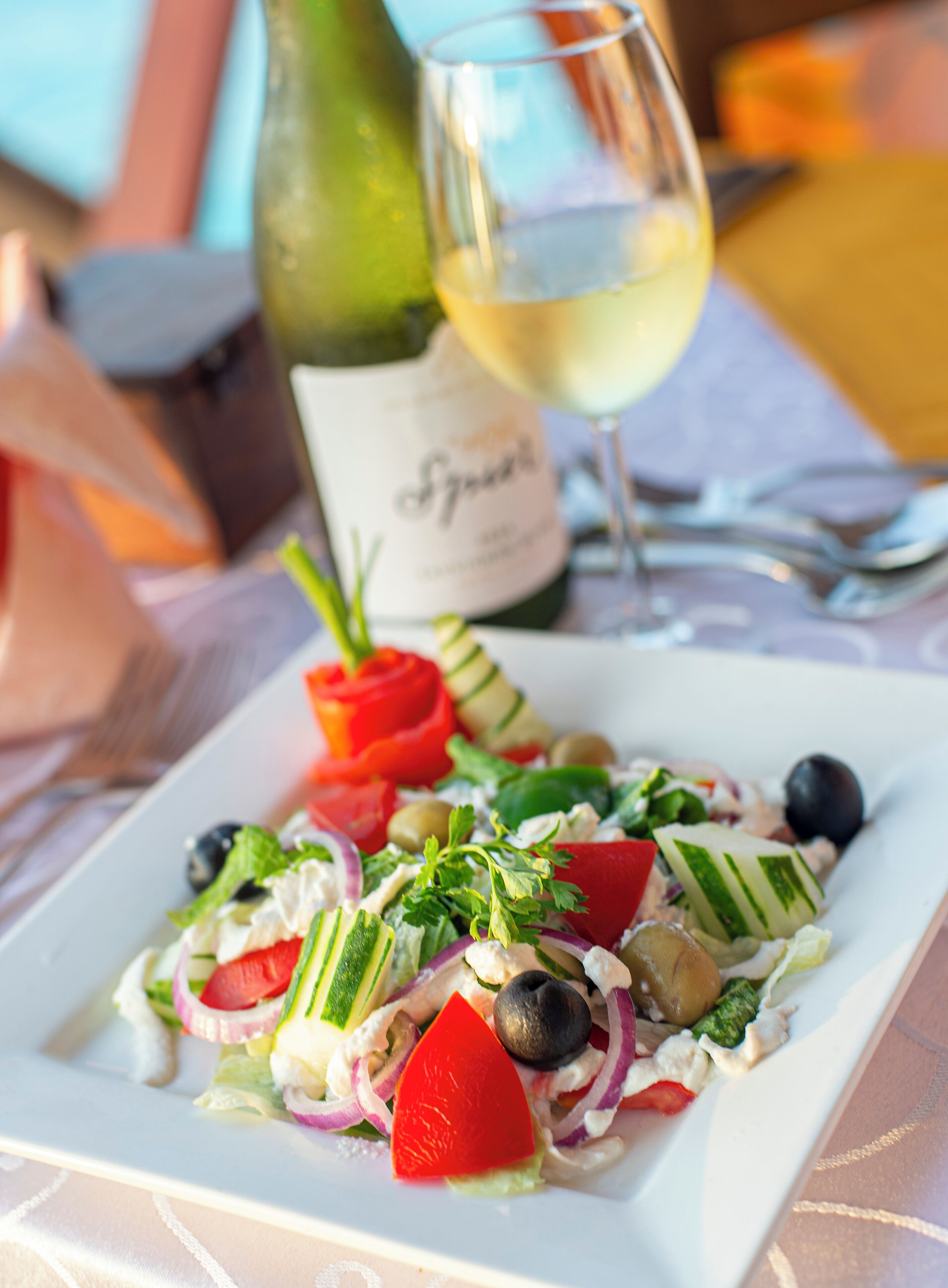 A plate of salad with various vegetables and a bottle of wine in the background.