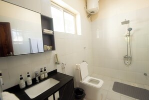 A bathroom with a white toilet, a sink with a black countertop, a mirror, and a shower area.