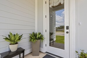 Welcome to a stylish entrance with a touch of greenery, featuring a modern door with a glass panel and keypad lock.