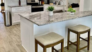 Una cocina moderna con gabinetes blancos, encimera de granito, electrodomésticos de acero inoxidable e iluminación colgante.