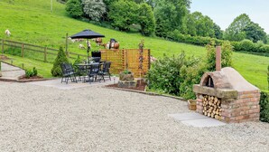 Een terras met een barbecue, zitplaatsen buiten en een houtoven.