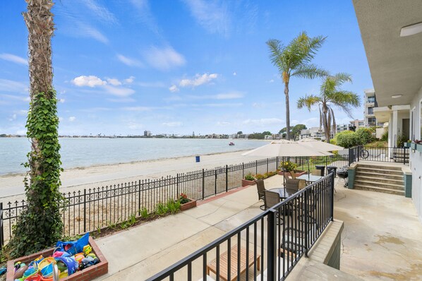 A balcony with a view of the beach, a palm tree, and a clear sky.