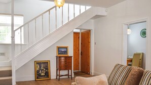 A staircase with white railings, a wooden floor, a framed picture on a small table, and a sofa with striped cushions. - 2 bedroom accommodation in Crosby, near Liverpool (Crosby, near Liverpool)