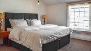 A bedroom with a bed, a nightstand, a lamp, and a window with blinds. - 2 bedroom accommodation in Crosby, near Liverpool (Crosby, near Liverpool)