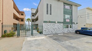 Un edificio residencial de varios pisos con fachada de piedra, entrada con reja y un coche azul estacionado en la entrada.