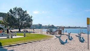 Una playa con un parque infantil, una torre de salvavidas y un cartel que indica zona de velocidad reducida para niños.