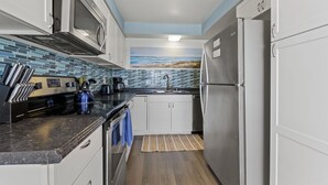 Una cocina compacta con armarios blancos, un refrigerador de acero inoxidable, un microondas y una cafetera.