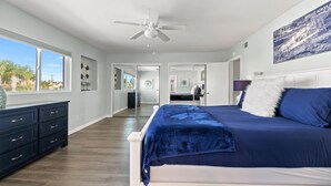 Un dormitorio con una cama grande, un ventilador de techo, un aparador y vistas al exterior.