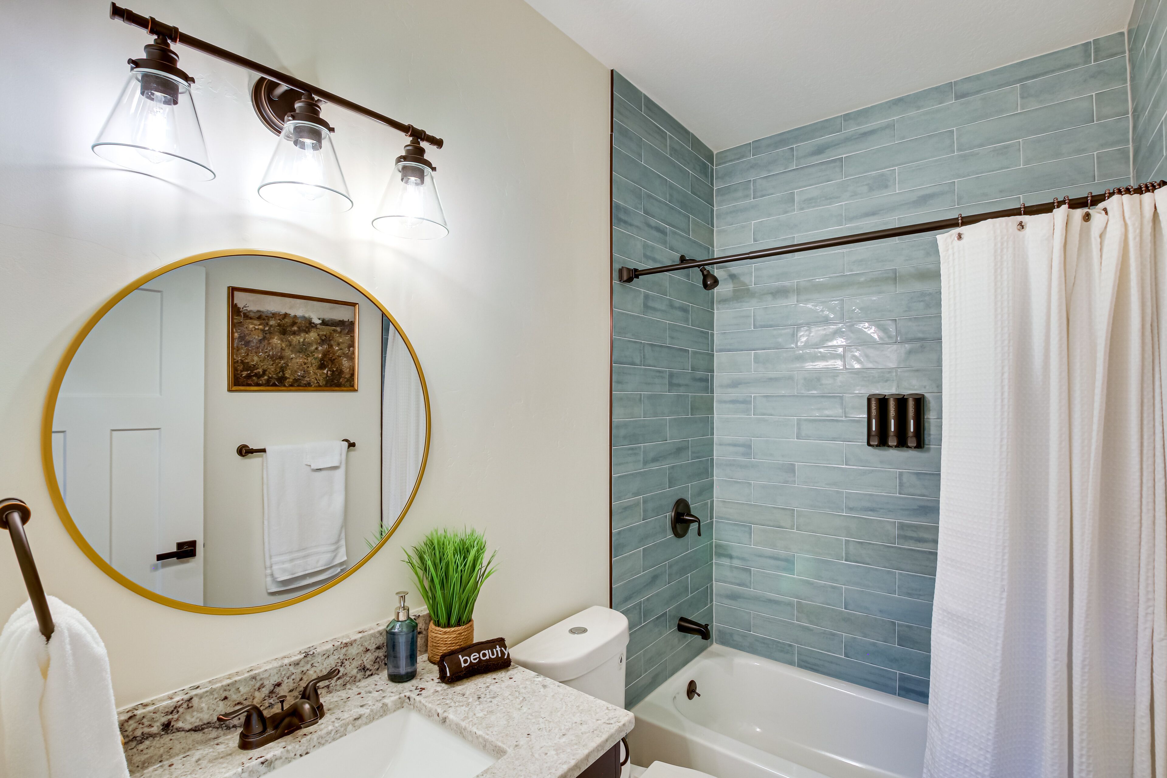 Un baño con lavamanos blanco, espejo redondo, inodoro y ducha con azulejos azules.