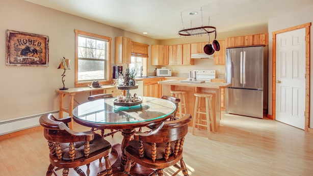 A modern kitchen with wooden cabinets, a stainless steel refrigerator, and a glass dining table. - Montana Vacation Rental: 32 Mi to Yellowstone! (Emigrant)