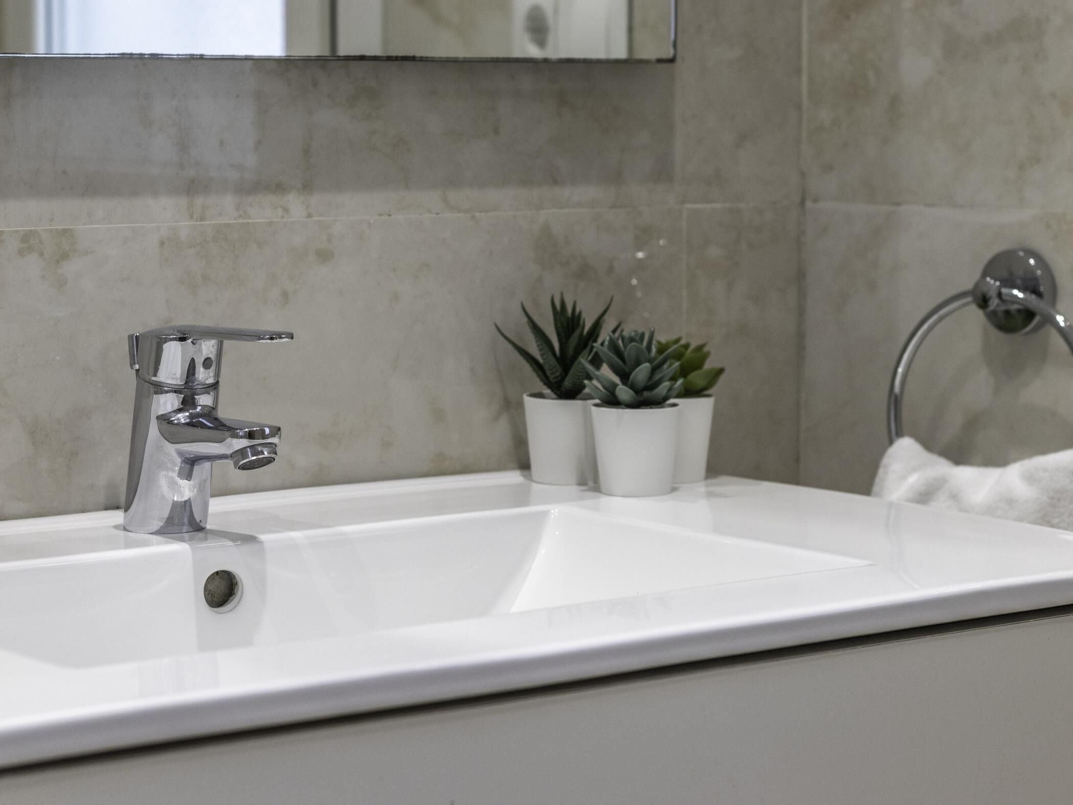 Un baño moderno con un lavamanos blanco, grifo cromado y un perchero para toallas.
