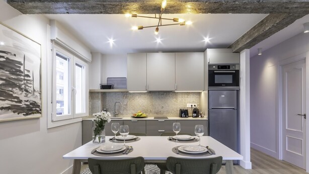 A modern kitchen with a dining area, featuring a large table set for four, a coffee machine, and a refrigerator. - Hola Bilbao! (Bilbao)