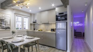 A modern kitchen with a dining area, featuring a large refrigerator, a built-in oven, and a neon sign. - Hola Bilbao! (Bilbao)