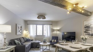 A modern living room with a sofa, a dining table set for two, a TV, and a large window with curtains. - Hola Bilbao! (Bilbao)
