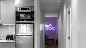 A modern kitchen with stainless steel appliances, a toaster, and a neon sign reading "hola BILBAO" in a hallway. - Hola Bilbao! (Bilbao)