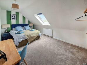 Un dormitorio con cama, escritorio, silla, radiador y tragaluz.