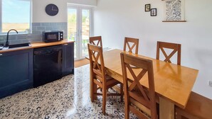 Une cuisine avec une table à manger et des chaises, une horloge et une fenêtre.