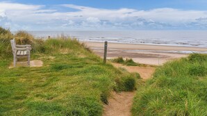 Un sentier qui longe la plage, avec un banc et un panneau indicateur.
