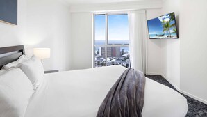 A hotel room with a large bed, a TV on the wall, and a window with a city view.