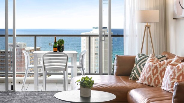 A balcony with a view of the sea, a brown leather sofa, a small table with a plant, and a white chair.