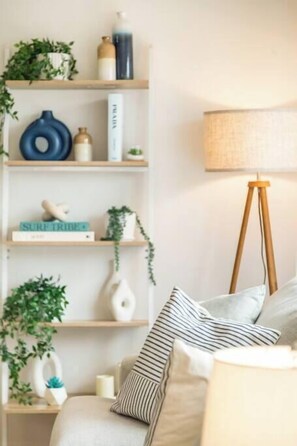 A living room with a sofa, striped pillows, a lamp, and shelves with plants and books. - Stunning Beach Oasis w/ Hot Tub (Carlsbad)