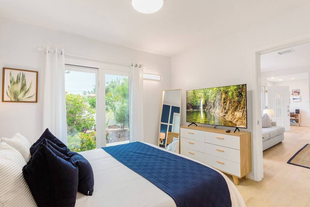 Ein Schlafzimmer mit Bett, Fernseher, Kommode und Blick auf Grünfläche.