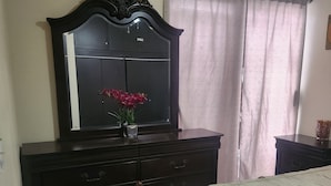 Ein Schlafzimmer mit einem Bett, einem Schminktisch mit Spiegel und einem Fenster mit Vorhängen.